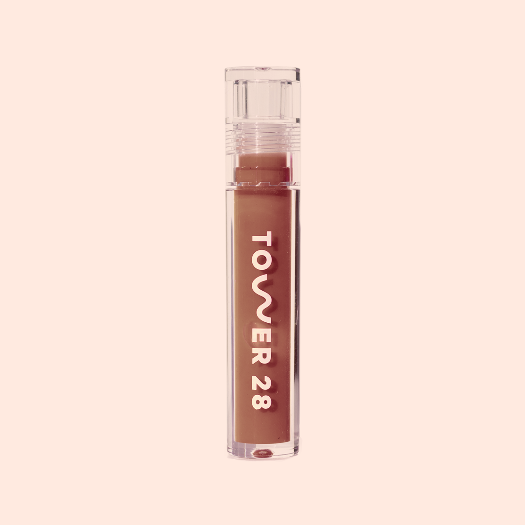 Photo of ShineOn Milky Lip Jelly in a slim acrylic tube with large "Tower 28" logo in shade Almond (a milky chocolat-brown shade) 